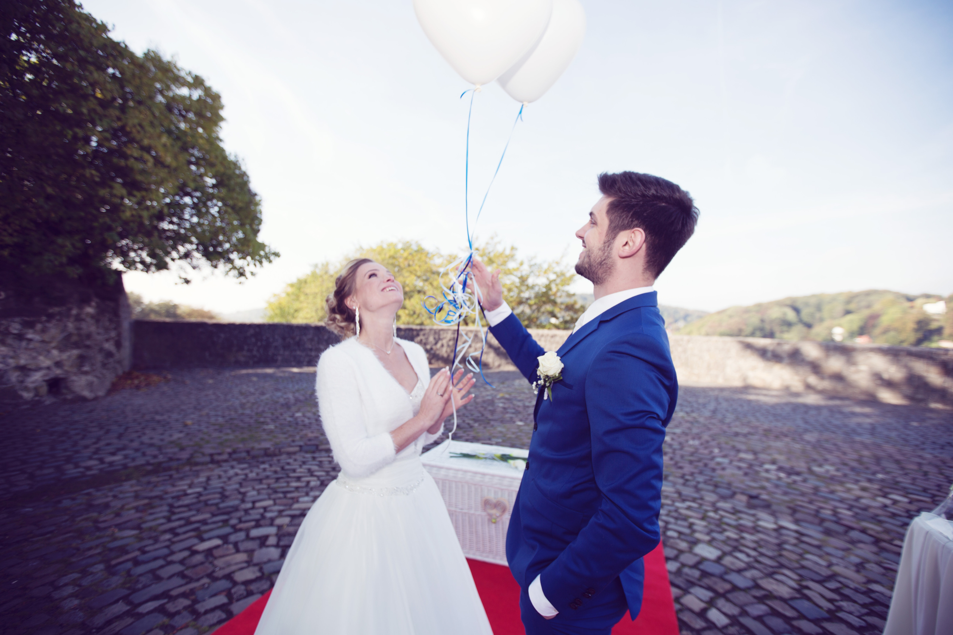 Hochzeitsfotograf Bielefeld – Brautpaar lässt weiße Luftballons steigen auf Burgmauer, Braut schaut lächelnd hoch, Herbststimmung