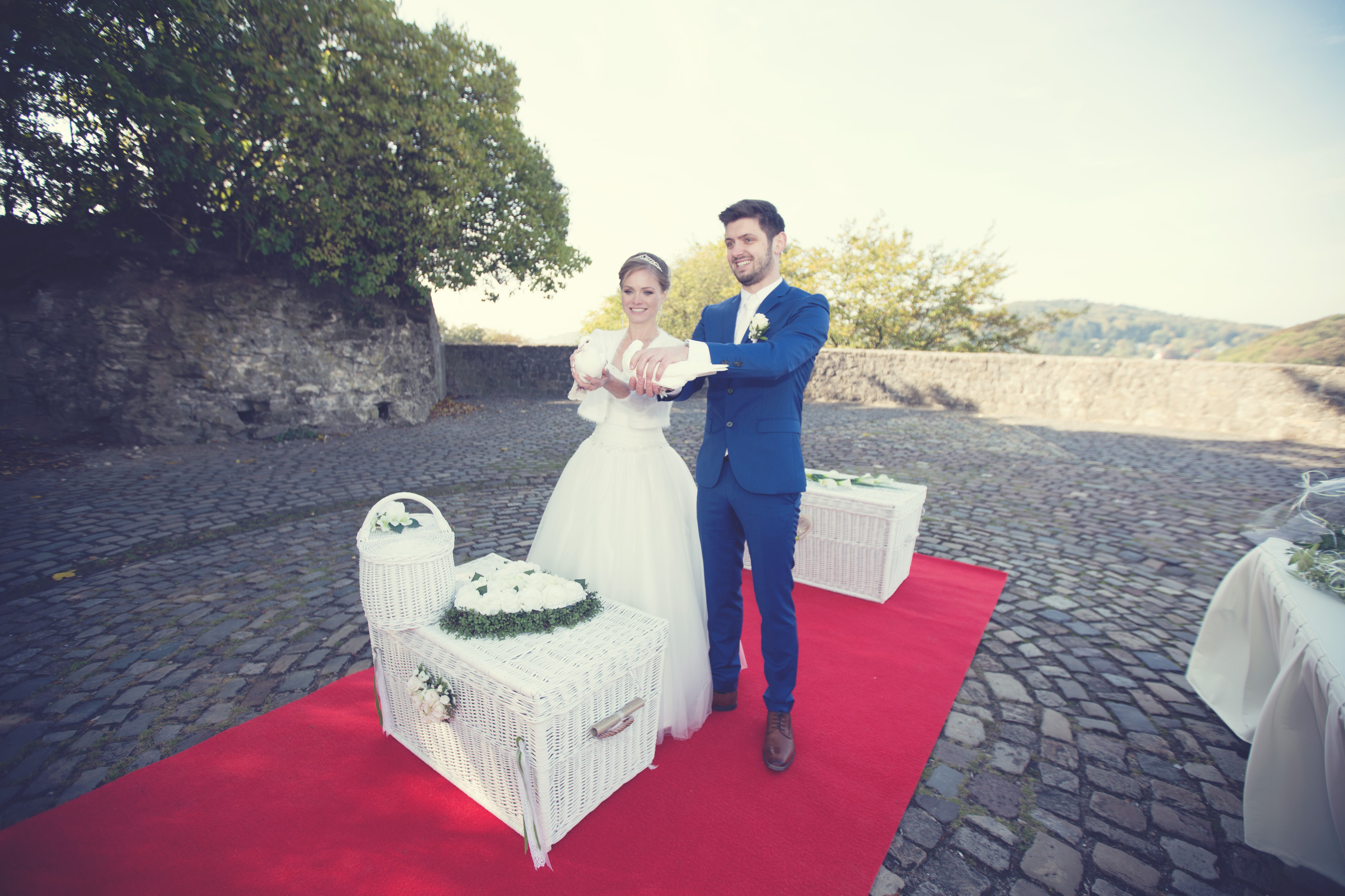 Hochzeitsfotograf Bielefeld – Brautpaar lässt weiße Tauben auf rotem Teppich auf Burgmauer frei, Herbststimmung
