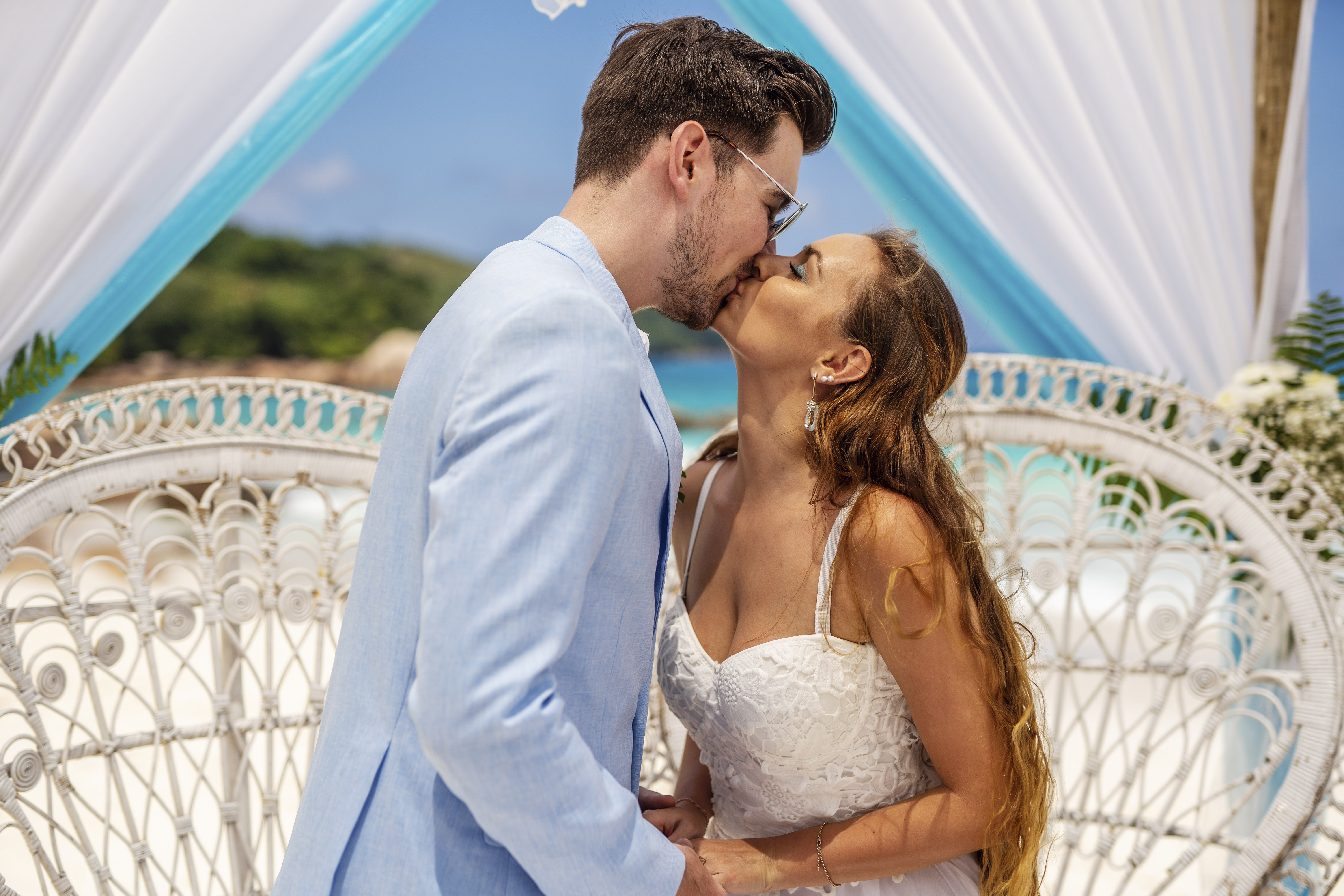 Hochzeitsfotograf Bielefeld – Destination Wedding Seychellen, Brautpaar küsst sich unter weißem Baldachin, türkises Meer, Anse Lazio