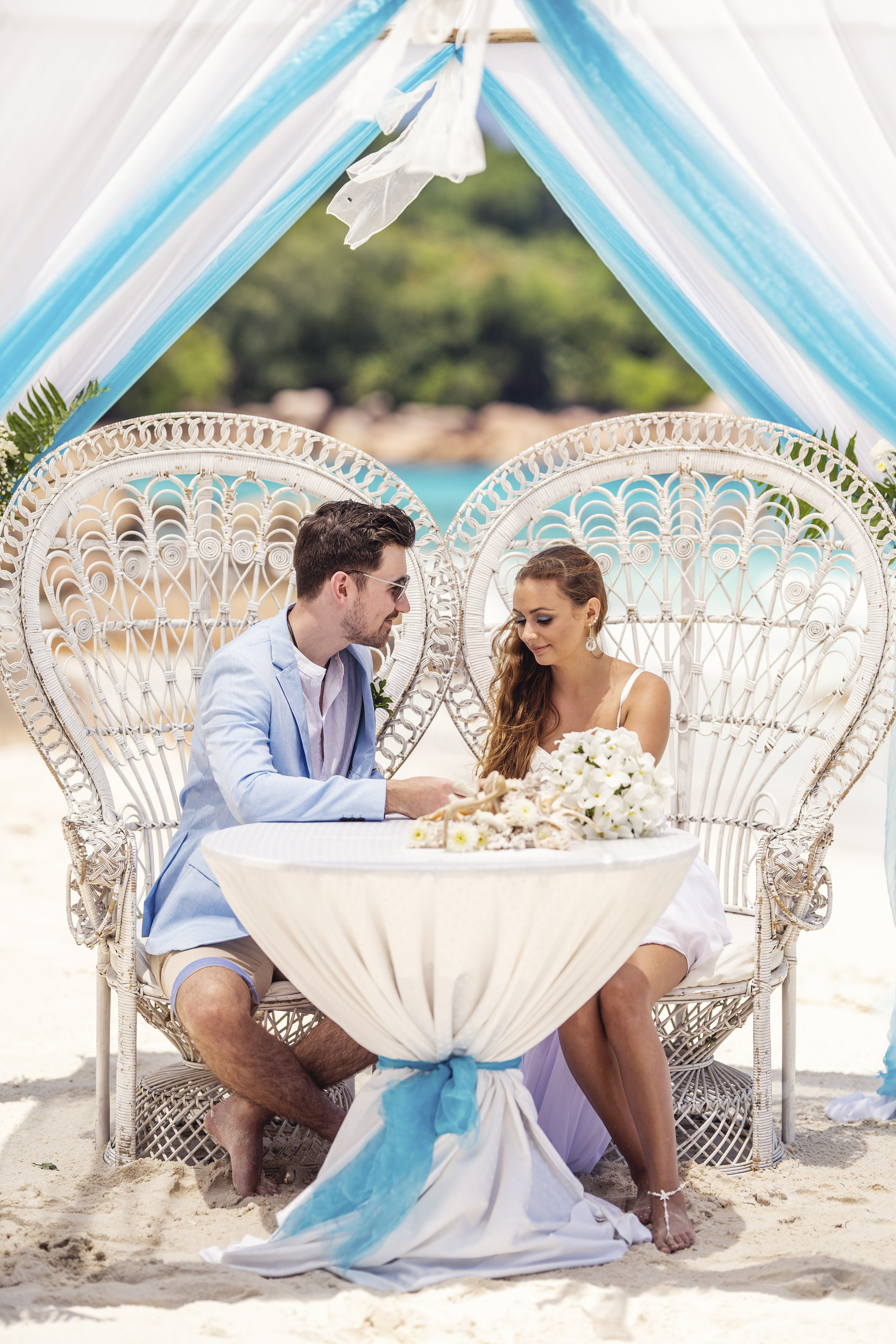 Hochzeitsfotograf Bielefeld – Hochzeit Seychellen, Brautpaar sitzt an gedecktem Tisch unter Baldachin, türkises Meer im Hintergrund