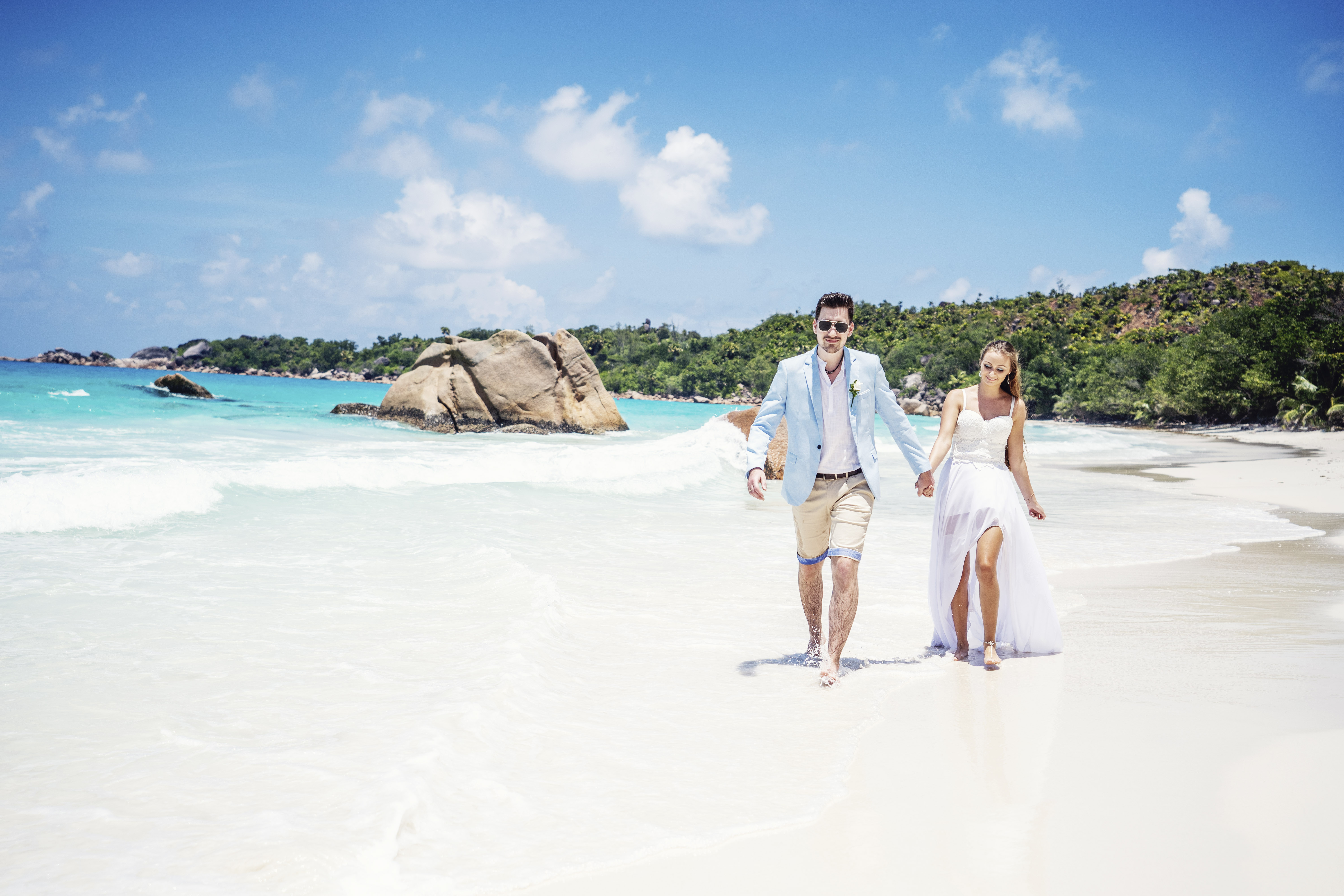 Hochzeitsfotograf Bielefeld – Hochzeitsfotografie Seychellen, Brautpaar geht Hand in Hand am weißen Strand, Granitfelsen