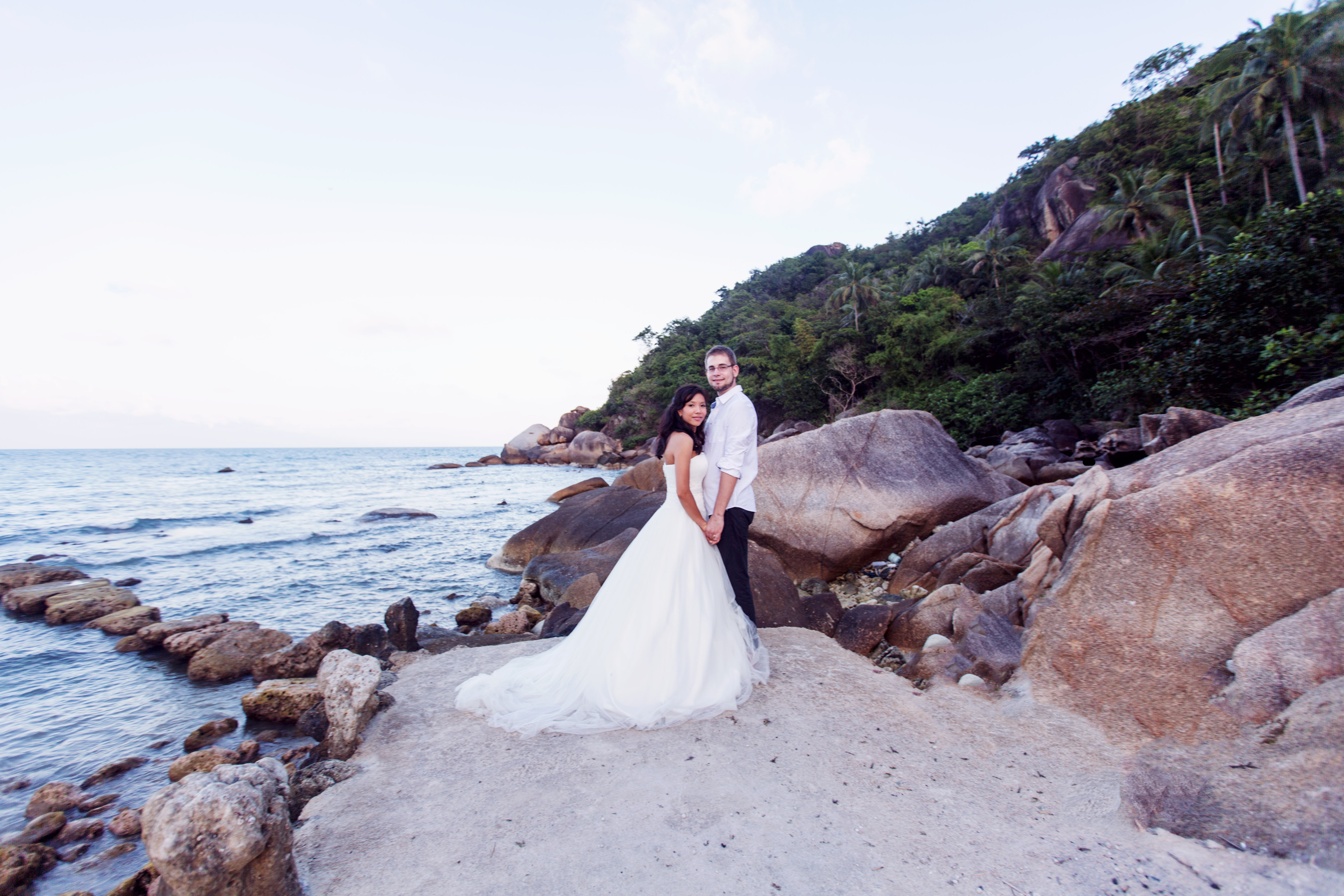 Hochzeitsfotograf Bielefeld – Hochzeitsfotos Koh Samui Thailand, Brautpaar am felsigen Strand, Braut im weißen Brautkleid mit langer Schleppe