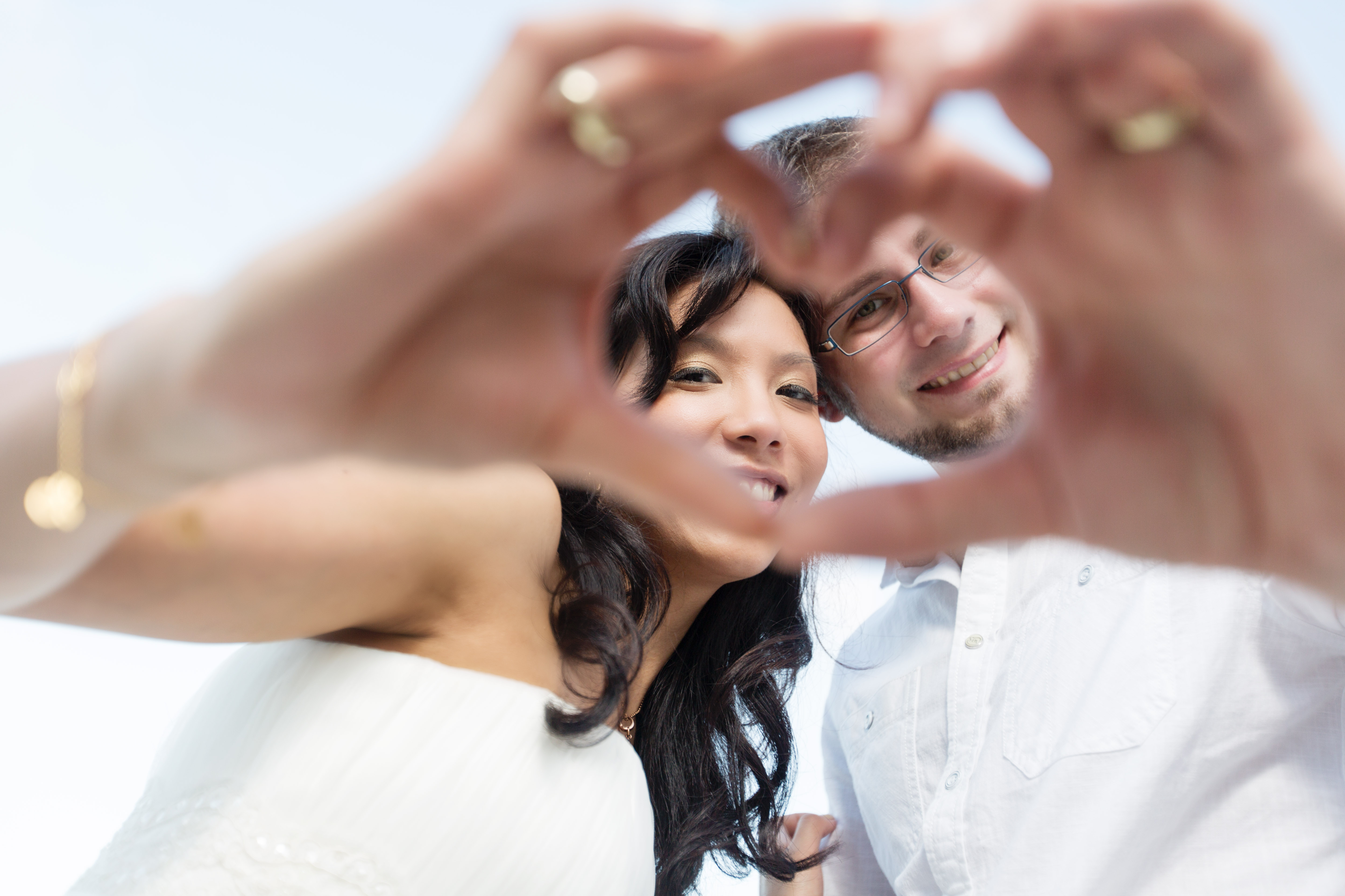 Hochzeitsfotograf Bielefeld – Destination Wedding Thailand, Brautpaar formt Herzgeste, Eheringe sichtbar, beide lächeln in die Kamera