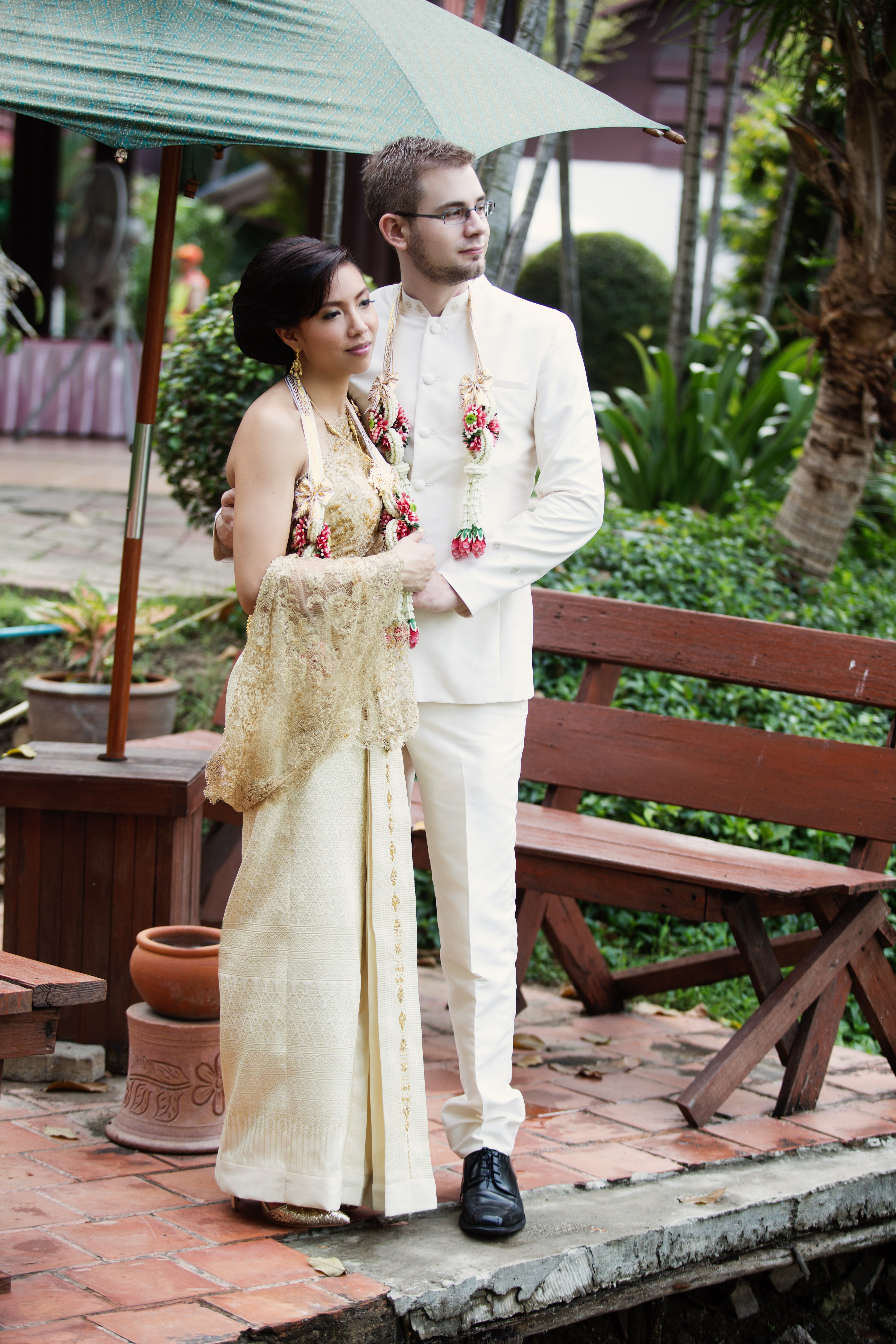 Hochzeitsfotograf Bielefeld – Buddhistische Hochzeit Bangkok, Brautpaar in traditioneller Festkleidung, Braut im goldenen Seidenkleid, Bräutigam mit Blumengirlanden